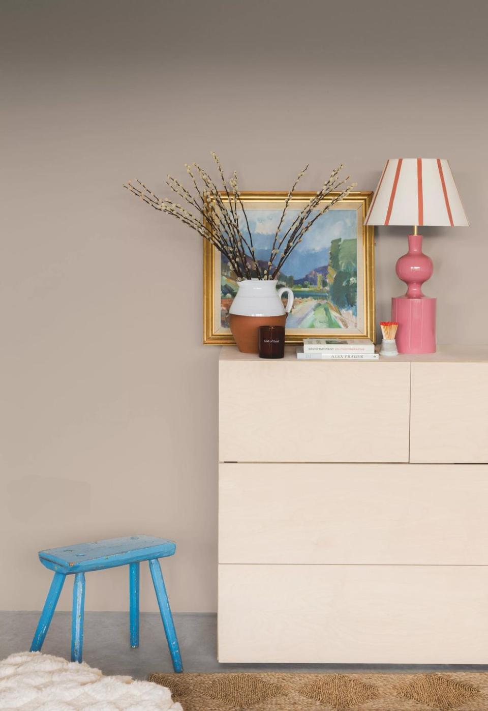 an off white dresser with a painting on it, faux branches in a vase and a pink lamp, with the colour amateur ceramics by coat paints on the wall