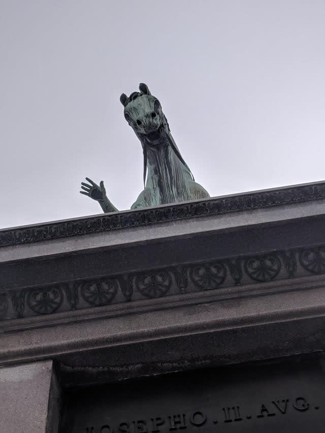 statue of a horse creeping from the side of the building that looks like it's waving with a human hand