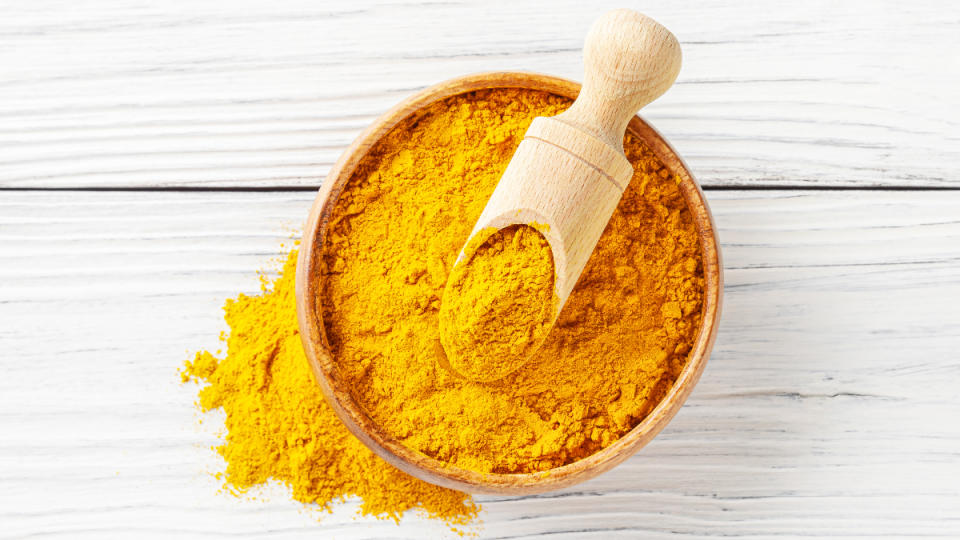 A bowl of ground turmeric, which is a heart disease prevention for women remedy, with a wooden spoon