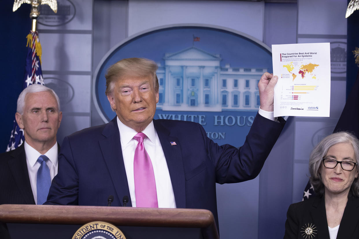 President Donald Trump, wearing a wry smile, and with Vice President Mike Pence at his side, holds up a sheaf of papers.