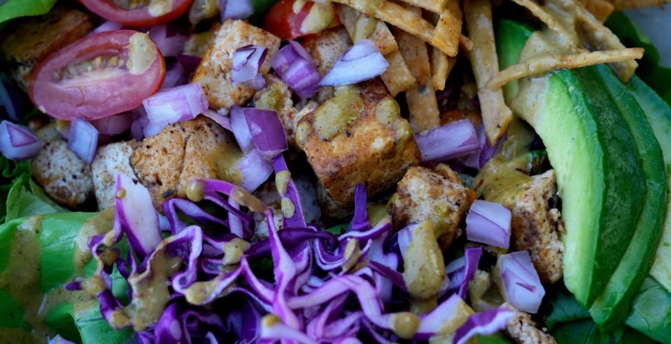 Avocado Greens. a dish at Basil & Bunny, features seasoned tofu, gourmet greens, red cabbage, tomato, avocado, red onions, lime, tortilla chips, topped with a spicy cashew dressing.