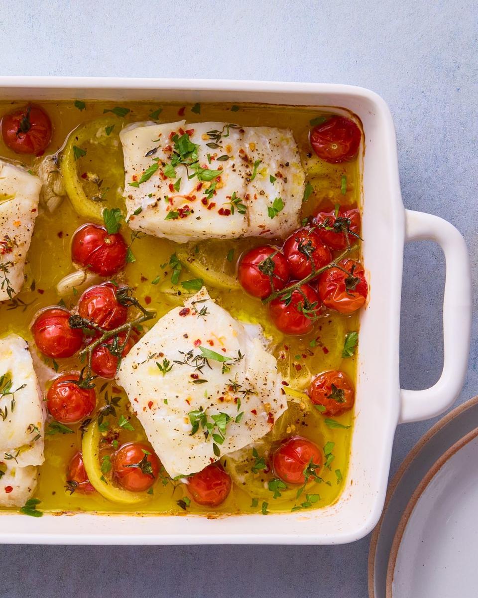 baked cod in a dish with lemon wedges and burst tomatoes