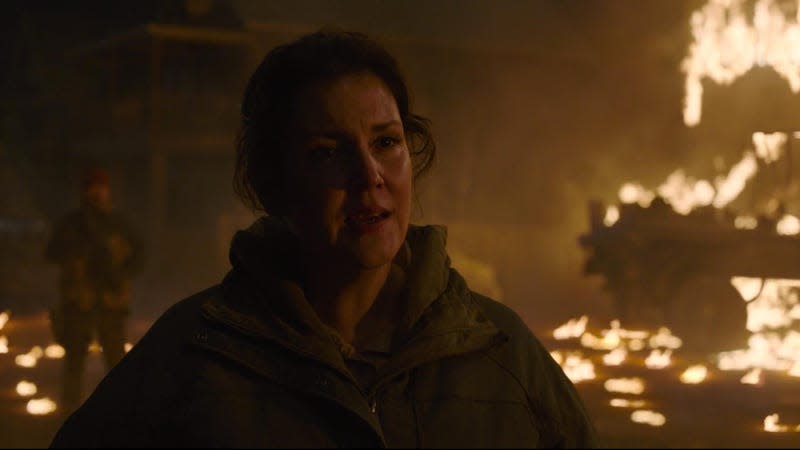 Melanie Lynskey as Kathleen stands with fiery wreckage behind her in a scene from HBO's The Last of Us.