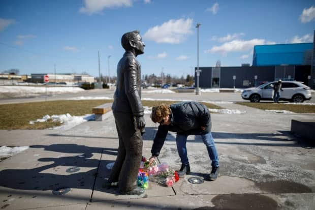 A woman places flowers at the foot of a statue depicting Walter Gretzky outside the Wayne Gretzky Sports Centre in Brantford, Ont., following news of his death.