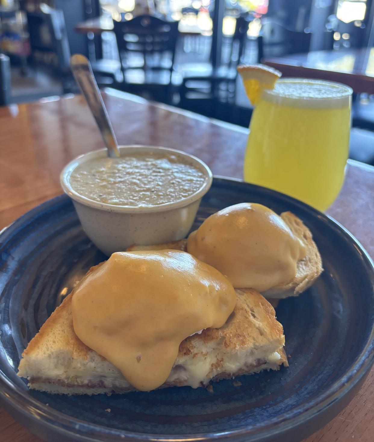 The Grilled Cheese Benedict, a special for January 2023, with a serving of black-truffle grits and a mimosa with fresh-squeezed orange juice.