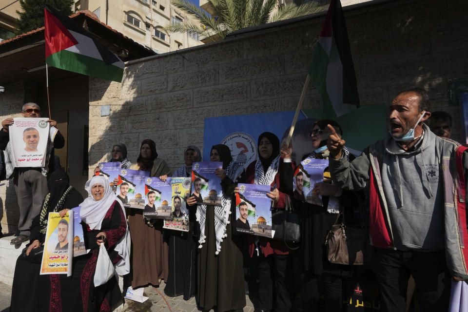 Palestinians wave their national flags while chant slogans as they hold pictures of a prisoner Nasser Abu Hamid during a protest in front of the International Committee of the Red Cross office, Tuesday, Dec. 20, 2022, in Gaza City, after he died of lung cancer in Israel. Abu Hamid was a former leader of the Al Aqsa Martyrs' Brigade, the armed wing of Palestinian President Mahmoud Abbas's Fatah party. He had been serving seven life sentences after being convicted in 2002 for involvement in the deaths of seven Israelis during the second Palestinian intifada, or uprising, against Israel's occupation in the early 2000s. (AP Photo/Adel Hana)