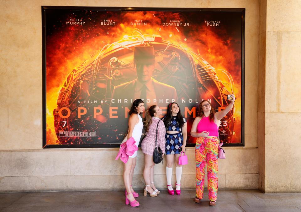 Moviegoers take a selfie in front of an "Oppenheimer" movie poster before they attended an advance screening of "Barbie" Thursday at AMC The Grove 14 theaters in Los Angeles.