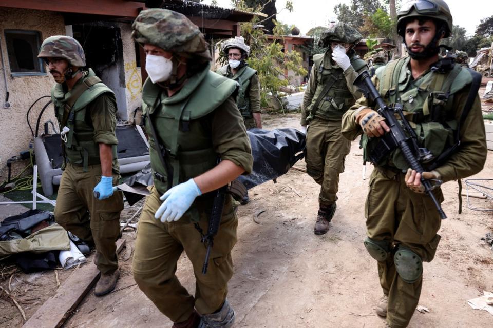 Israeli soldiers carry a body in Kfar Aza (Reuters)