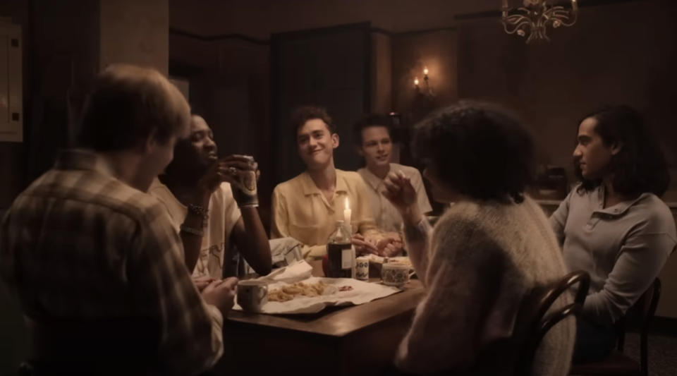 A group of six people are seated around a dimly lit table, sharing a meal and conversing