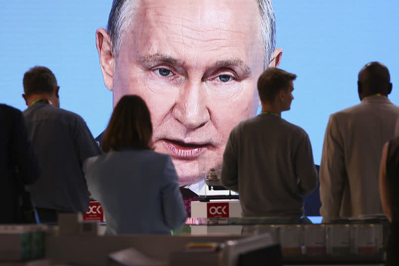 People sit near a TV screen broadcasting Russian President Vladimir Putin's speech in St Petersburg, July 2023