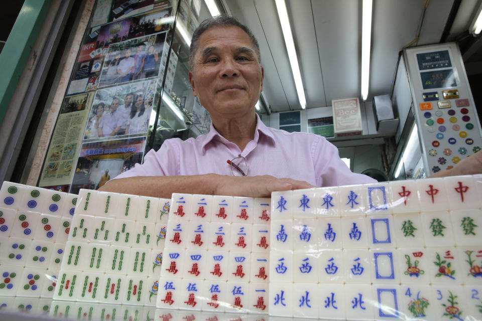 In this April 18, 2019, photo, Cheung Shun-king, 65-year-old mahjong game tile maker, poses with his tiles in his shop in Kowloon's old neighborhood of Hong Kong. Hand-carved mahjong tiles is a dying art in Hong Kong. But Cheung is trying to revive the heritage/raise people's interest by organizing hand-craved tile class to keep the tradition alive. (AP Photo/Kin Cheung)