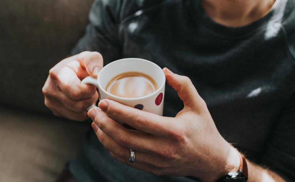 Man holding a cup of tea in two hands, in a spotty mug.