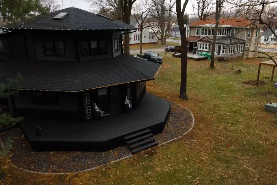 An exterior view of the house shows its black painting, roof detailing, and a neighbour's house.