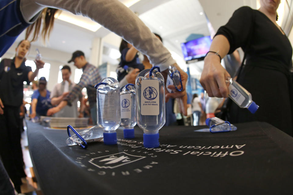 Fans reach for hand sanitizer before the start of the Denver Nuggets vs Dallas Mavericks NBA basketball game, Wednesday, March11, 2020, in Dallas. The Mavericks supplied the sanitizer for free. (AP Photo/Ron Jenkins)