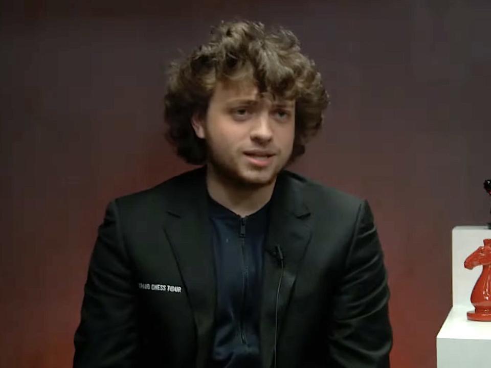 Hans Niemann, in a black sports jacket on a chess backdrop, speaks during an interview.