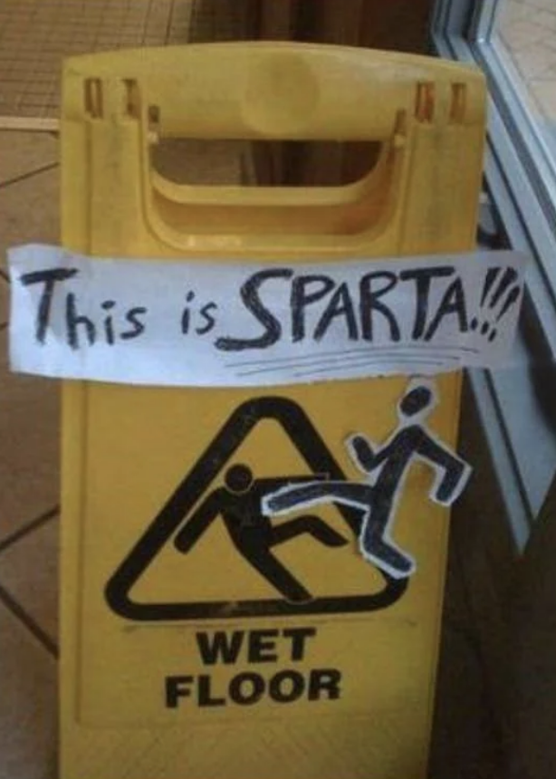 Wet floor sign with handwritten "This is SPARTA!" taped above the caution symbol