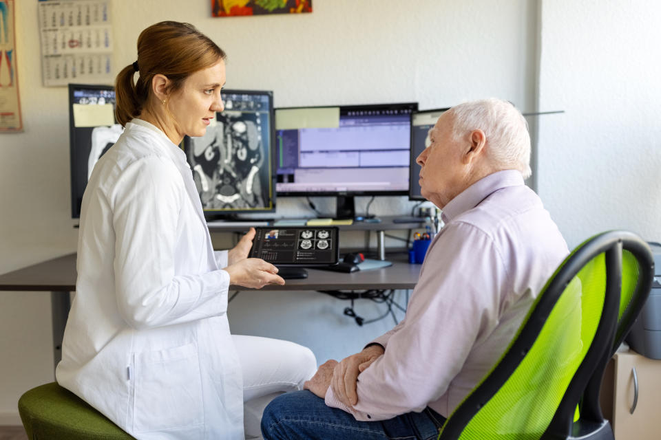 Female doctor talking with senior male patient showing CAT scan results in hospital. Neurologist discussing MRI scan results with senior man in clinic.