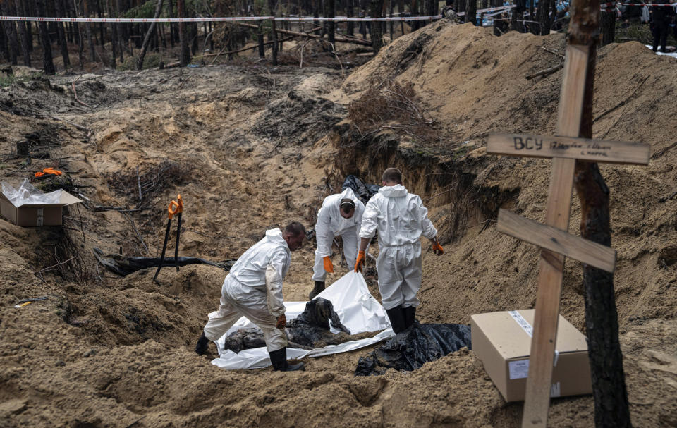 Experts work around a body during an exhumation in the recently retaken area of Izium, Ukraine, Friday, Sept. 16, 2022. Ukrainian authorities discovered a mass burial site near the recaptured city of Izium that contained hundreds of graves. It was not clear who was buried in many of the plots or how all of them died, though witnesses and a Ukrainian investigator said some were shot and others were killed by artillery fire, mines or airstrikes. (AP Photo/Evgeniy Maloletka)