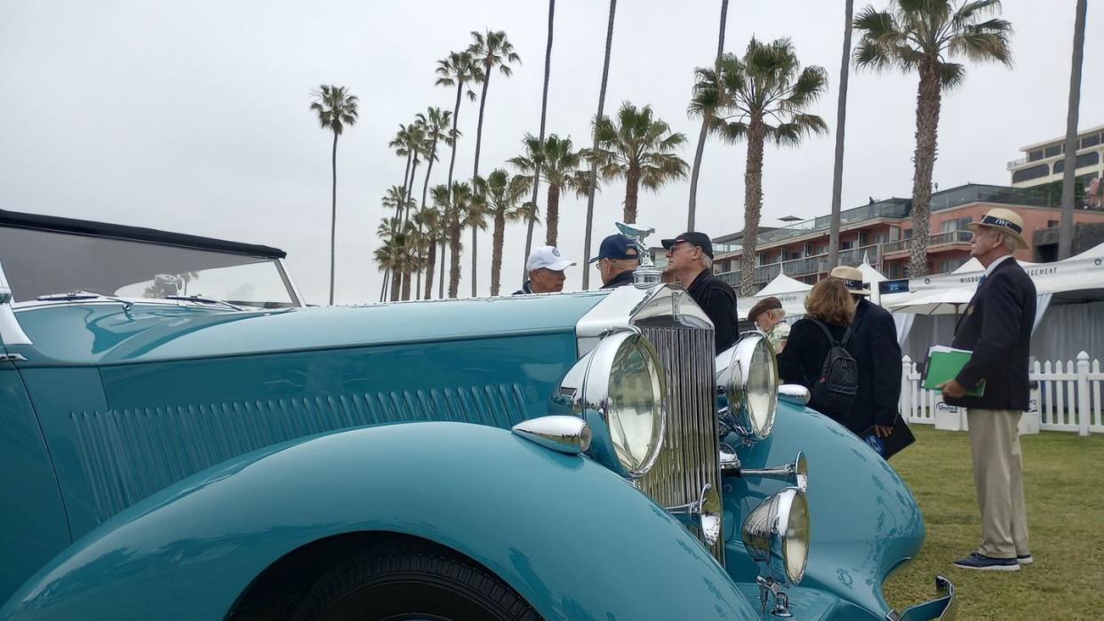 a group of people standing around a blue car