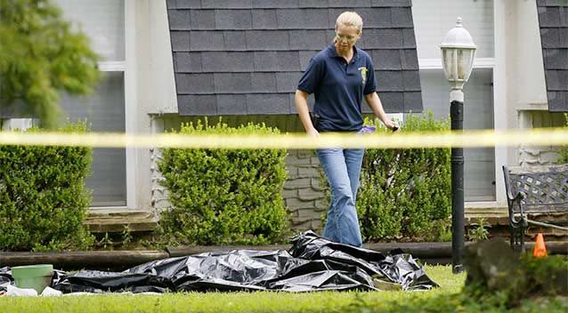 An investigator walks past a tarp covering a body in the front yard of a house in Broken Arrow, where five family members were discovered stabbed to death. Photo: AP