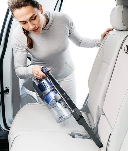 A model using the Shark vacuum in handheld mode to clean the interior of a car