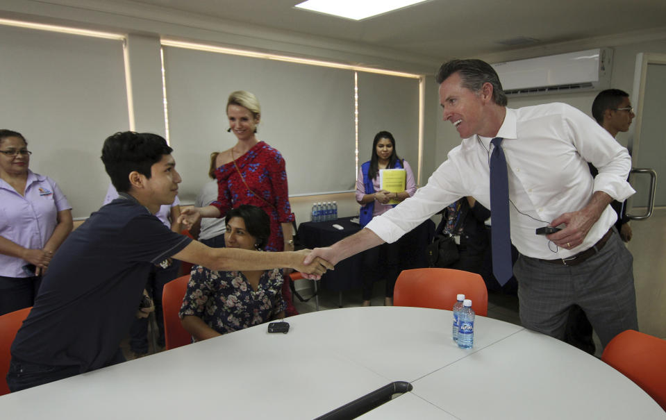 California Gov. Gavin Newsom, right, and his wife, Jennifer Siebel Newsom greet Byron Daniel, 17, a young Salvadoran, who had fled El Salvador due to the harassment of gang members looking to recruit him, during their visit to La Chacra Immigration Center in San Salvador, El Salvador, Monday, April 8, 2019. The Migrant Care Center processes deported migrants. (AP Photo/Salvador Melendez)