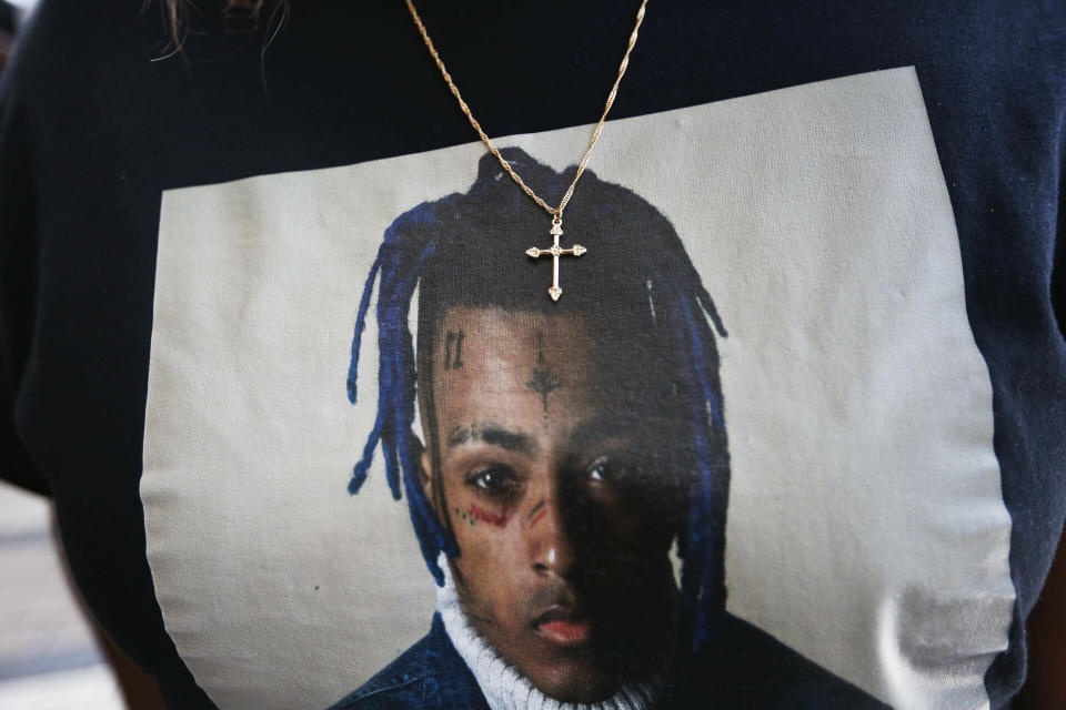 FILE- In this June 27, 2018, file photo a fan wears a cross around her neck dangling on a t-shirt in remembrance before she enters a memorial for the rapper, XXXTentacion in Sunrise, Fla. More than four years after gunmen killed the emerging rap star XXXTentacion during a robbery outside a South Florida motorcycle shop, three suspects are about to go on trial. Jury selection begins Wednesday, Jan. 18, 2023, in Fort Lauderdale. Alleged shooter Michael Boatwright and his accused accomplices, Dedrick Williams and Trayvon Newsome, could all receive life sentences if convicted of first-degree murder. (AP Photo/Brynn Anderson, File)