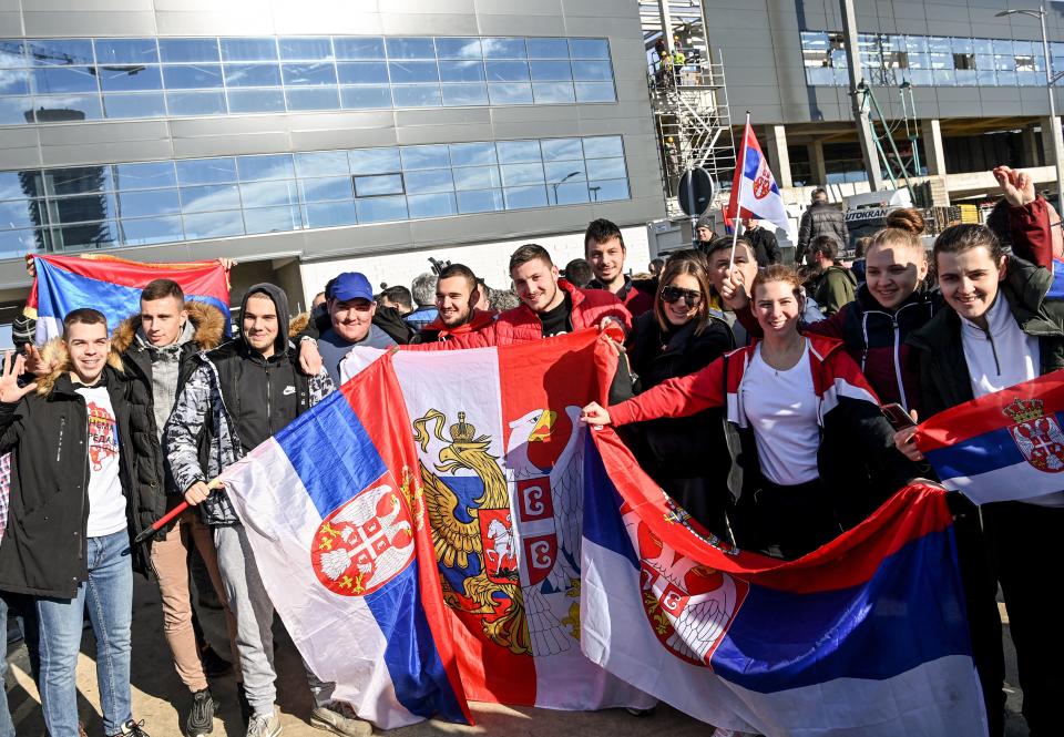 People holds Serbian national flags as they pose while waiting outside the VIP exit of Belgrade's international airport on January 17, 2022, for Tennis world number one Novak Djokovic's arrival after his deportation from Australia over his coronavirus vaccination status. - The unvaccinated nine-time Australian Open champion Djokovic flew out of Melbourne after his last-gasp court bid to stay in the country failed. The visa saga cast a dark shadow over the opening Grand Slam of the year and few players were willing to give him public backing as the controversy dragged out. (Photo by ANDREJ ISAKOVIC / AFP) (Photo by ANDREJ ISAKOVIC/AFP via Getty Images)