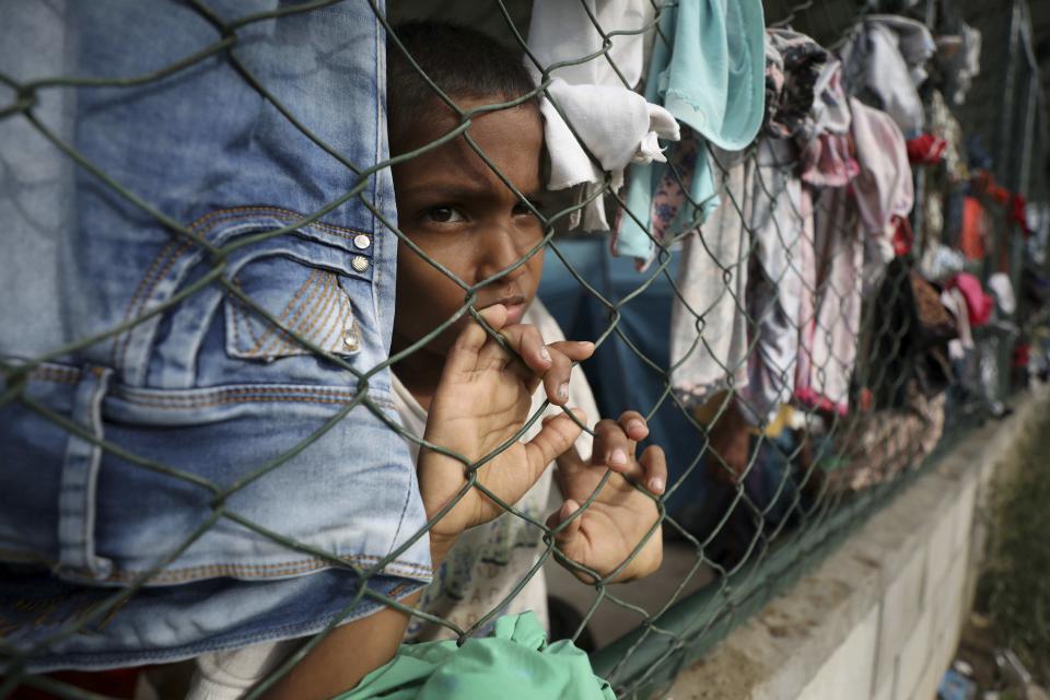 A child looks through a fence of a shelter at a community center in Arauquita, Colombia, Thursday, March 25, 2021, on the border with Venezuela. Thousands of Venezuelans are seeking shelter in Colombia this week following clashes between Venezuela's military and a Colombian armed group in a community along the nations' shared border. (AP Photo/Fernando Vergara)