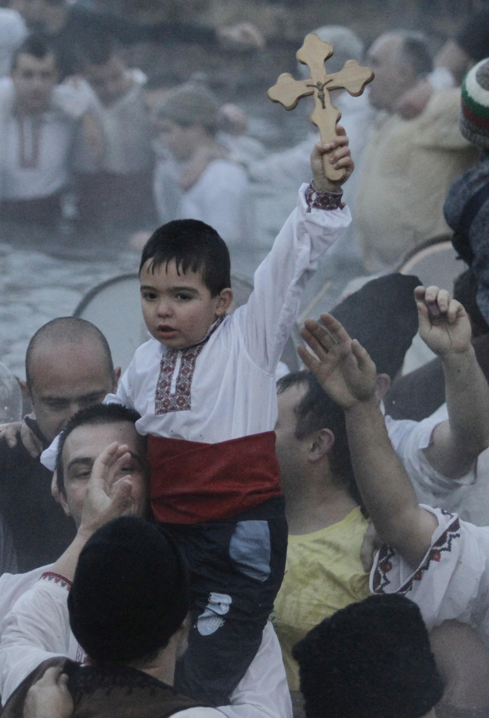 A boy holds a cross as believers sing and dance in the icy waters of the river Tundzha to celebrate Epiphany day in the town of Kalofer, Bulgaria, Monday, Jan. 6, 2014. Traditionally, an Eastern Orthodox priest throws a cross in the river and it is believed that the one who retrieves it will be healthy through the year. (AP Photo/Valentina Petrova)