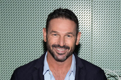 Jason smiling in a casual suit in front of a mint green, patterned, wall.