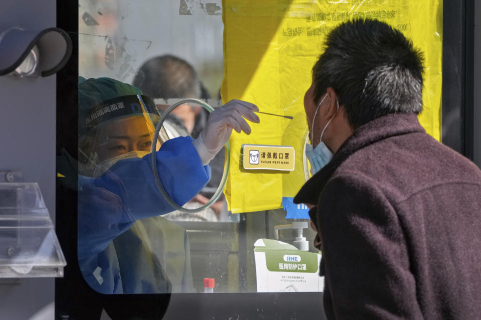 A medical worker in protective gear collects a sample from a man at a coronavirus testing site setup along a pedestrian walkway in Beijing on Sunday, Oct. 16, 2022. The overarching theme emerging from China's ongoing Communist Party congress is one of continuity, not change. The weeklong meeting is expected to reappoint Xi Jinping as leader, reaffirm a commitment to his policies for the next five years and possibly elevate his status even further as one of the most powerful leaders in China's modern history. (AP Photo/Andy Wong)