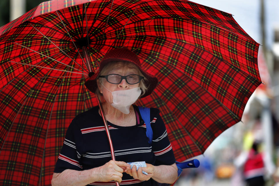 An elderly woman wearing a mask against the spread of the new coronavirus walks with an umbrella at the San Gregorio Atlapulco market in Mexico City, Monday, April 20, 2020. (AP Photo/Marco Ugarte)