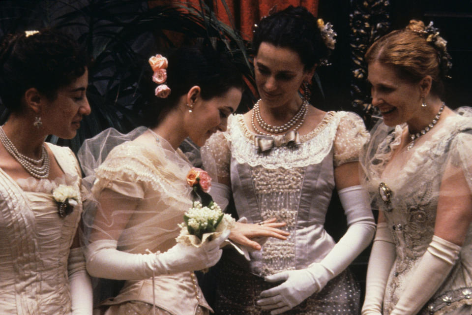 four women in 1800s style dresses with long gloves and flowers in their hair