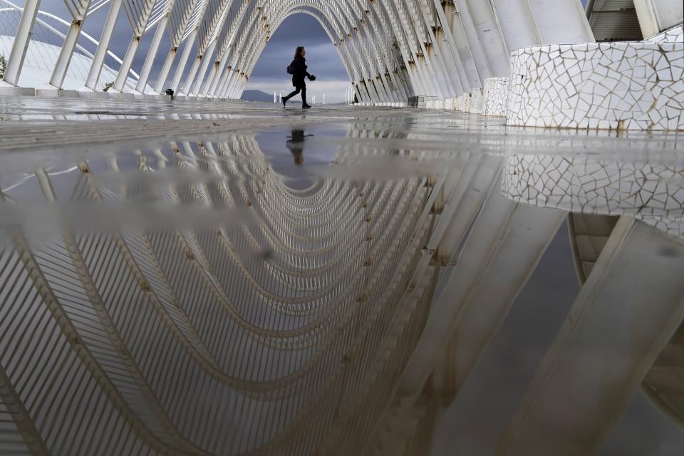 A woman is reflected on rain water as she walks inside the modern Agora walkway at the main Olympic complex in Athens, Thursday, Oct. 14, 2021. Greece's authorities are in full activation mode as the wet and stormy weather system named "Ballos" reached the country bringing thunder, lightning and showers, and causing fluctuations in the power supply. (AP Photo/Thanassis Stavrakis)