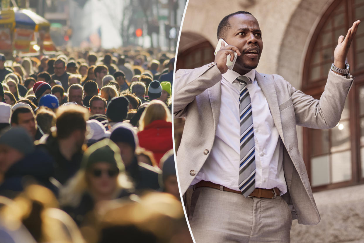 Crowd of people walking busy New York City street backlit, with a man talking on a cell phone