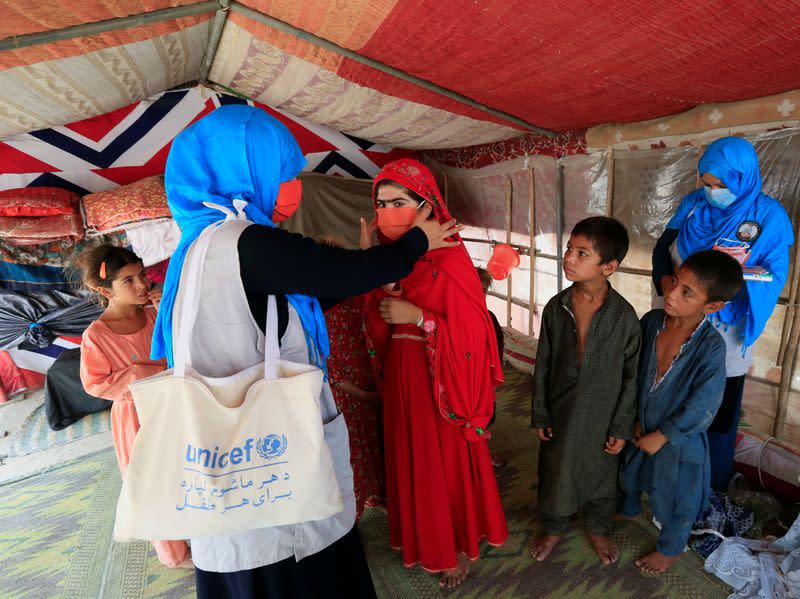 FILE PHOTO: A UNICEF worker helps an internally displaced girl put on a face mask at a makeshift camp, amid the coronavirus disease (COVID-19) outbreak, in Jalalabad