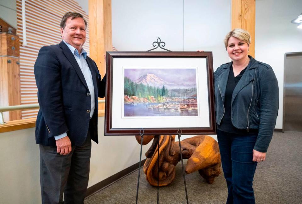 Tim Ham, left, and Mayor of Gig Harbor Tracie Markley, right, pose for a portrait with Afghan artist Abdul’s painting of Gig Harbor that he created while living in hiding with his family from the Taliban in Afghanistan, in Gig Harbor on March 29, 2023. Cheyenne Boone/Cheyenne Boone/The News Tribune