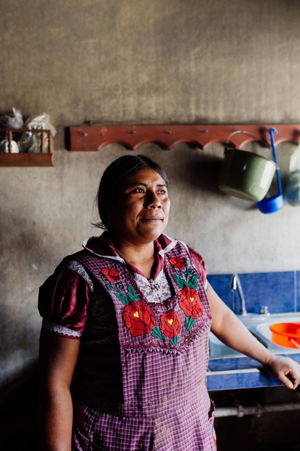 One of the women of the red clay village gazes out the window from the kitchen of her household, where the smell of roasting chicken, bell peppers, and onions wafts through the air.