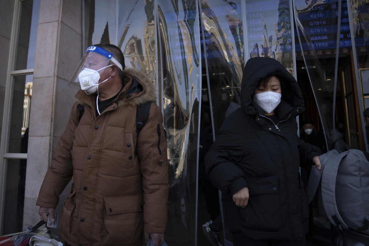 Travelers wearing face masks and a face shield walk out of an exit of the Beijing Railway Station in Beijing, Saturday, Jan. 14, 2023. Millions of Chinese are expected to travel during the Lunar New Year holiday period this year. (AP Photo/Mark Schiefelbein)