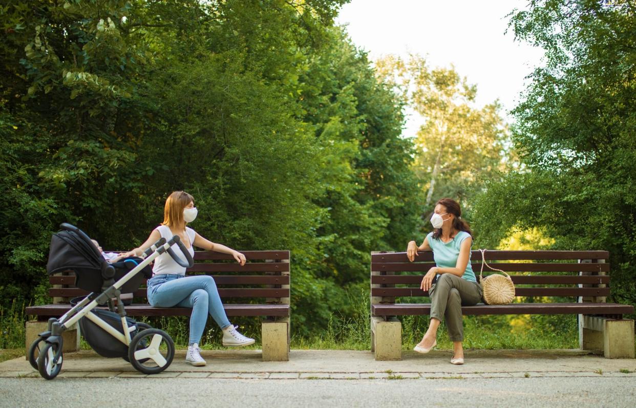 An image of two women sitting in a park with masks on.