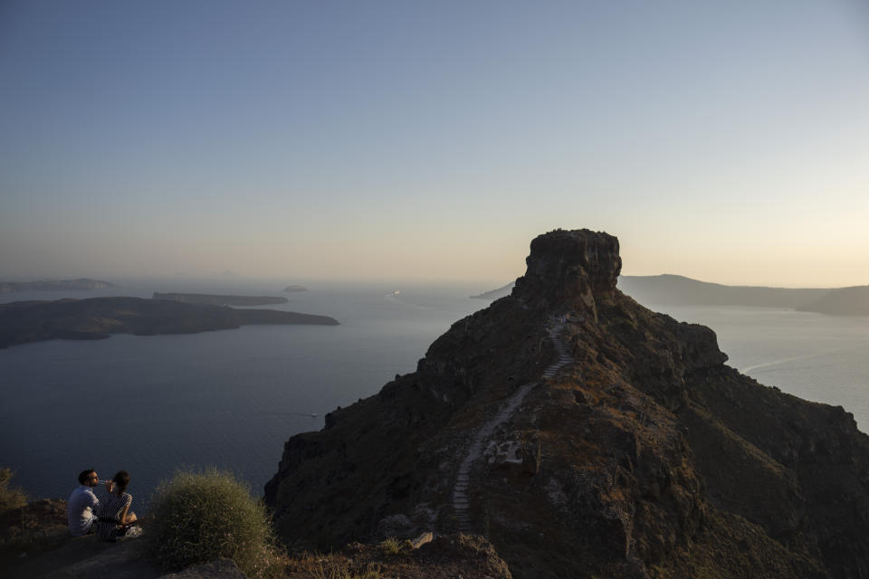 Una pareja disfruta de las vistas en el promontorio rocoso de Skaros en la isla griega de Santorini el 15 de junio del 2022. El Monasterio Católico de Santa Catalina fue fundado en Skaros en 1596, pero debió ser trasladado a otro Thira tras un terremodo. Hoy cuenta con más de una docena de monjas de clausura dedicadas a la oración y el recogimiento. (AP Photo/Petros Giannakouris)