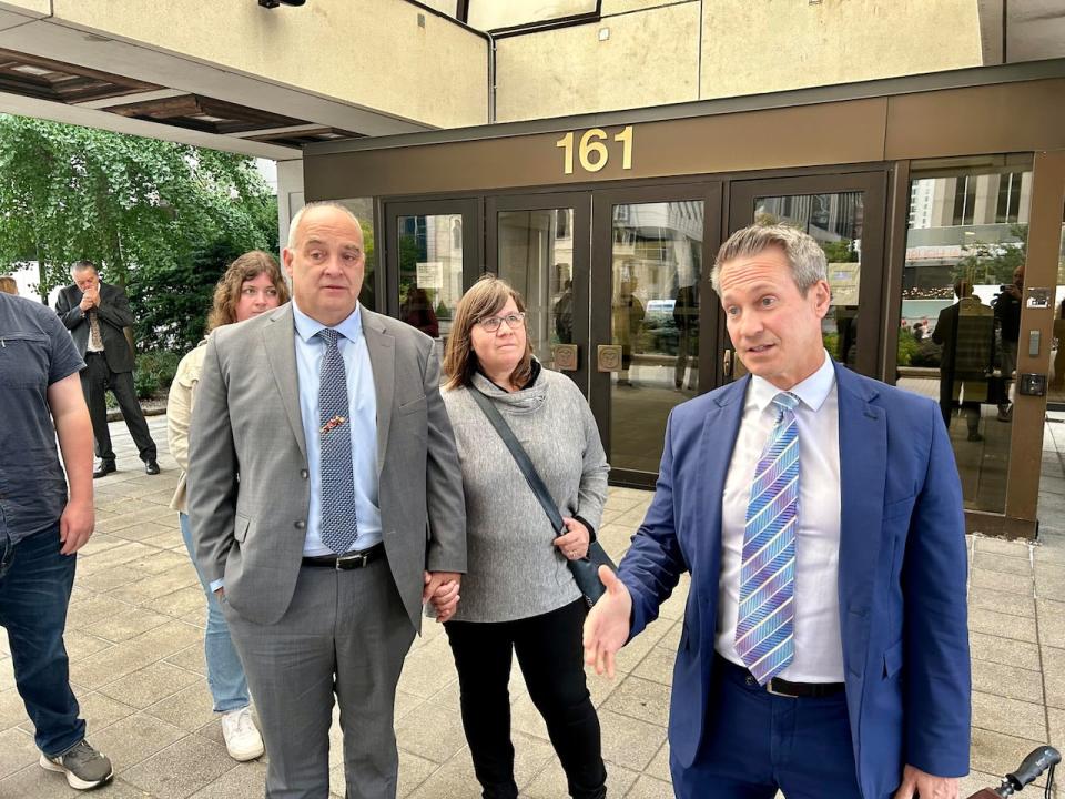 Lawyer Joshua Clarke, right, speaks to reporters outside the Ottawa Courthouse on Wednesday as Capt. Greg Wright, left, and his wife stand by. 