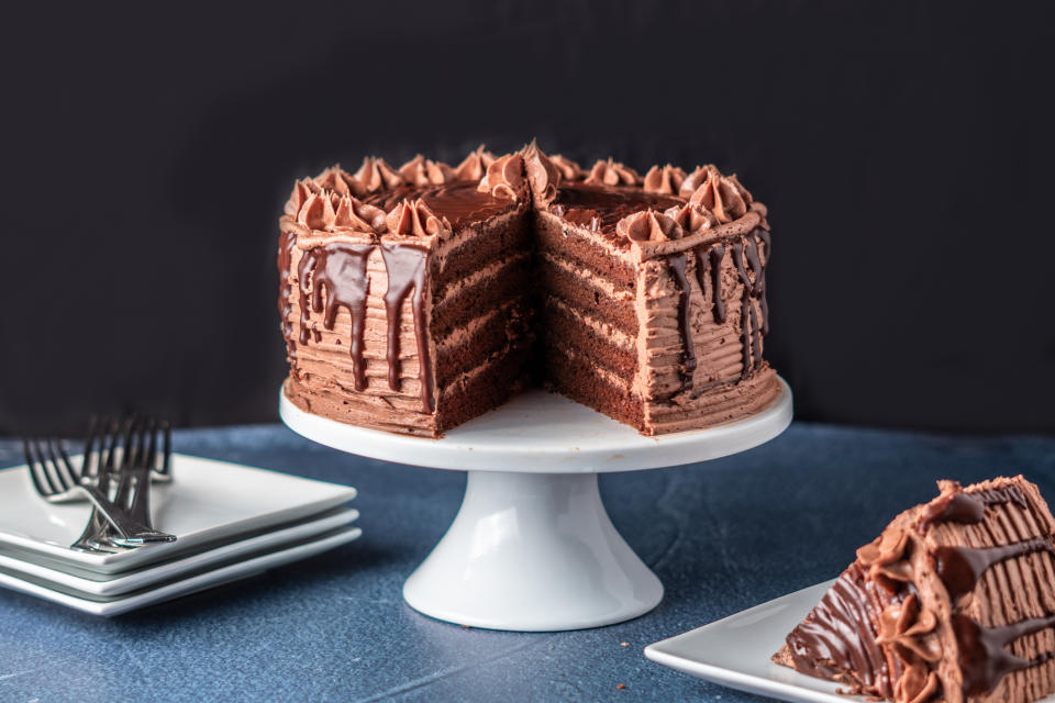 Chocolate cake with a slice cut out, on a stand, with plates and forks beside it