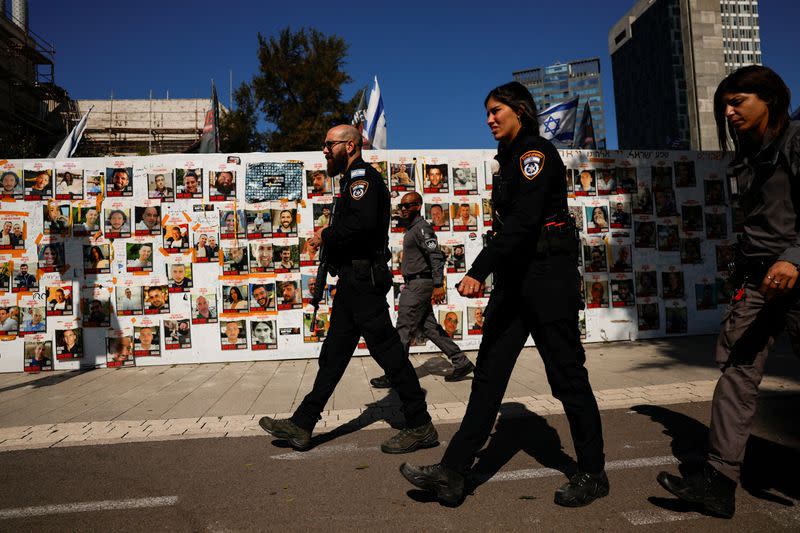 Israeli police officers walk past a board displaying pictures of hostages kidnapped in the deadly October 7 attack, in Tel Aviv