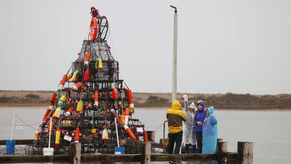 Guowei Yang takes a photo of Fang Yang, left, Clara Wang, Lan (no last name given) in the rain at Morro Bay’s South T-Pier next to a Christmas crab pot display on Dec. 20, 2023.