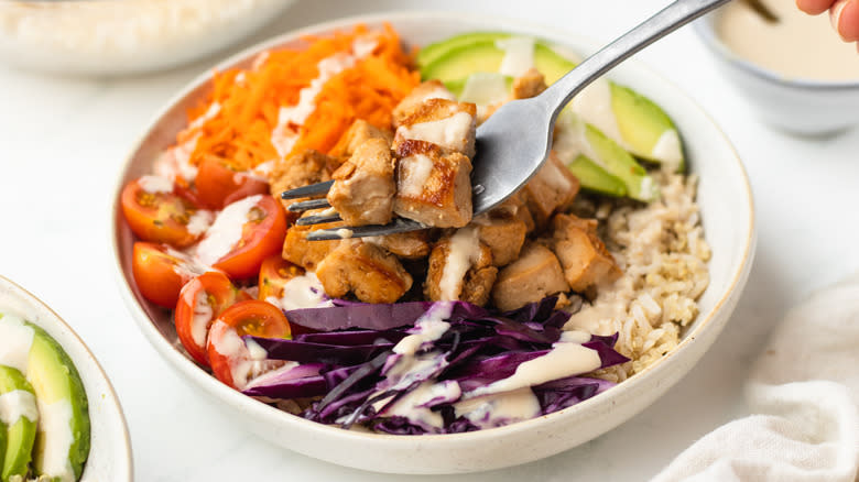 Tofu on a fork over a grain bowl