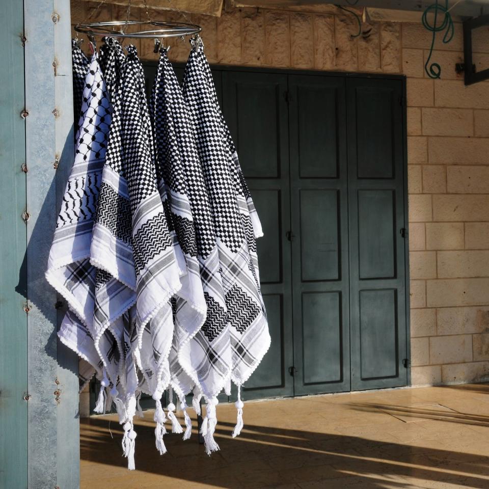 Black and white checkered scarves hanging on display outside in a shaded area, with a building featuring closed dark green doors in the background