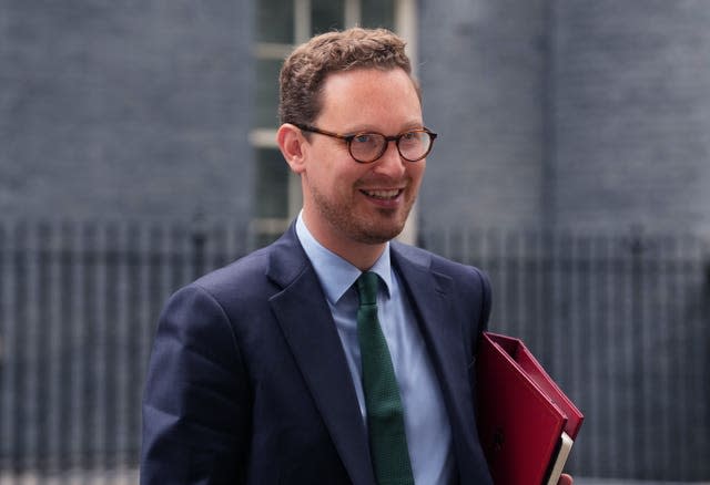 Treasury Chief Secretary Darren Jones in front of black railing holding a red file