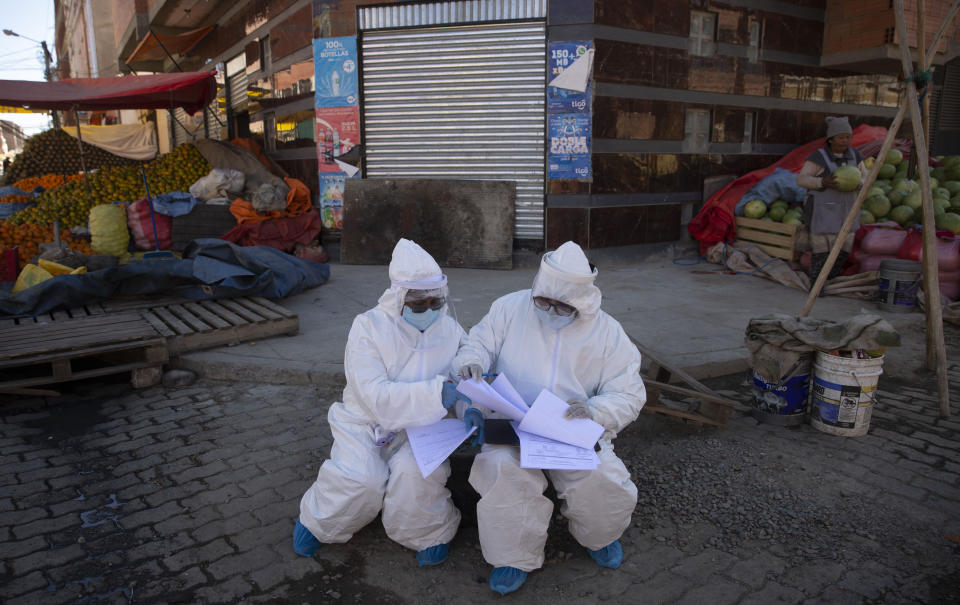 Healthcare workers dressed in full protective gear organize their documents of data they have collected during a house-to-house new coronavirus testing drive, ringed by a produce market in the Villa Dolores neighborhood of El Alto, Bolivia, Saturday, July 18, 2020. (AP Photo/Juan Karita)